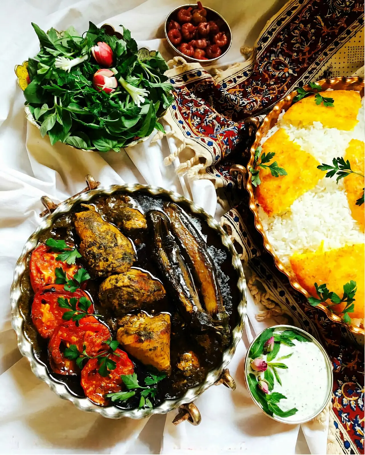 سفره‌ای با خورش سبز گیلانی، بادمجان و گوجه، دیس برنج با ته دیگ زعفرانی و بشقاب سبزی خوردن