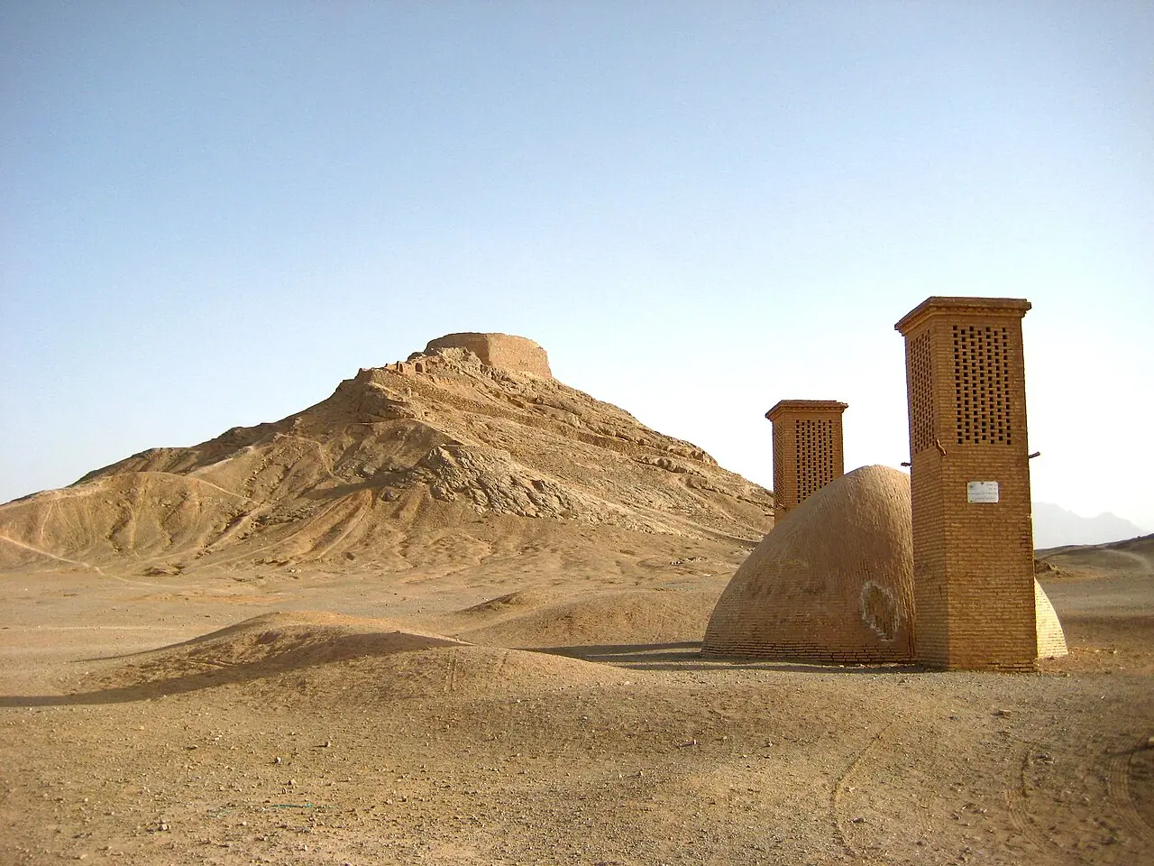 دخمه‌ی زرتشتیان بر فراز تپه‌ای خاکی و بادگیرها و گنبد یک بنای خشتی در پای آن