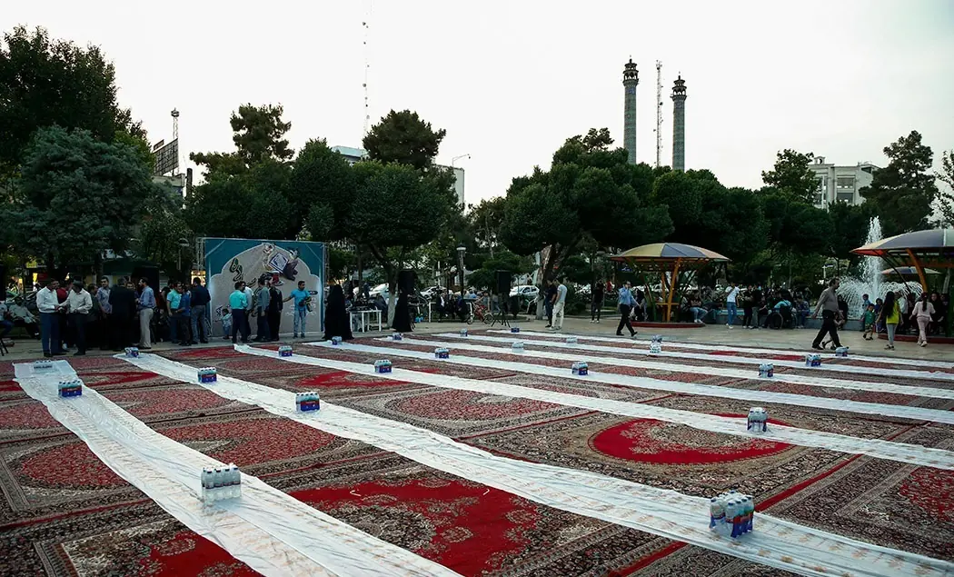 ردیف سفره‌های بلند افطار روی فرش‌ها در میدانی در تهران پیش از رسیدن مهمانان