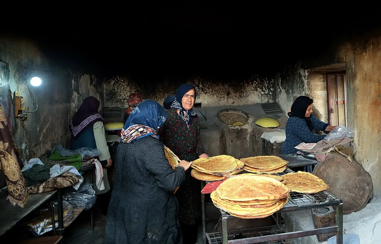 چند زن در یک نانوایی سنتی روستایی کنار هم مشغول آماده کردن و پختن نان‌اند