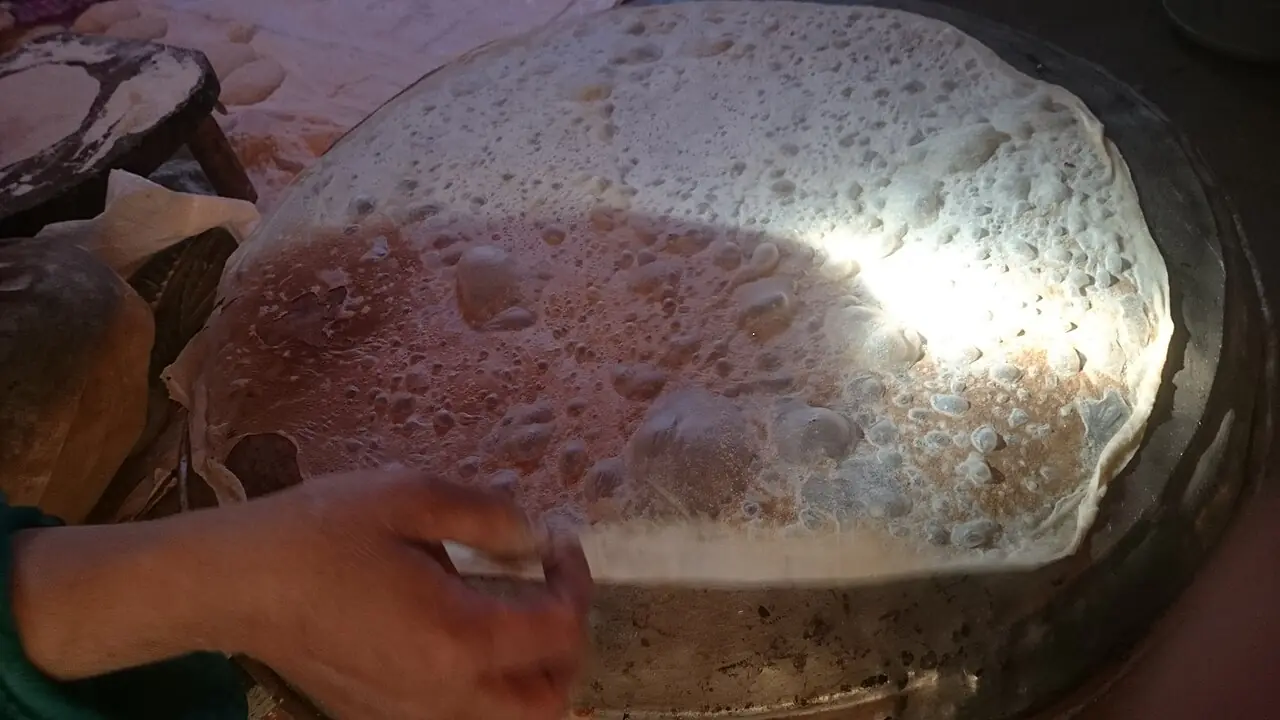 نان نازک و پهنی که روی ساج داغ پخته می‌شود و دست نان‌پز در کنار آن