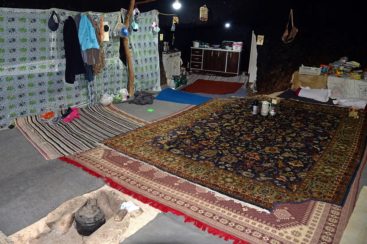 درون یک اتاق دستکند در میمند با فرش و گلیم روی زمین و سقف سیاه‌شده از دود