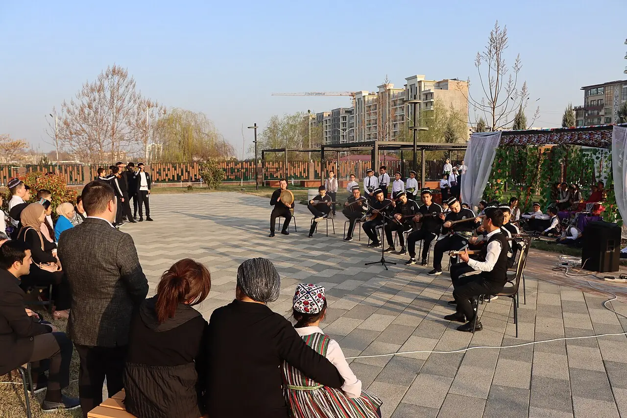 گروهی از نوازندگان جوان با رباب در میدانی باز اجرا می‌کنند و تماشاگران روی صندلی نشسته‌اند
