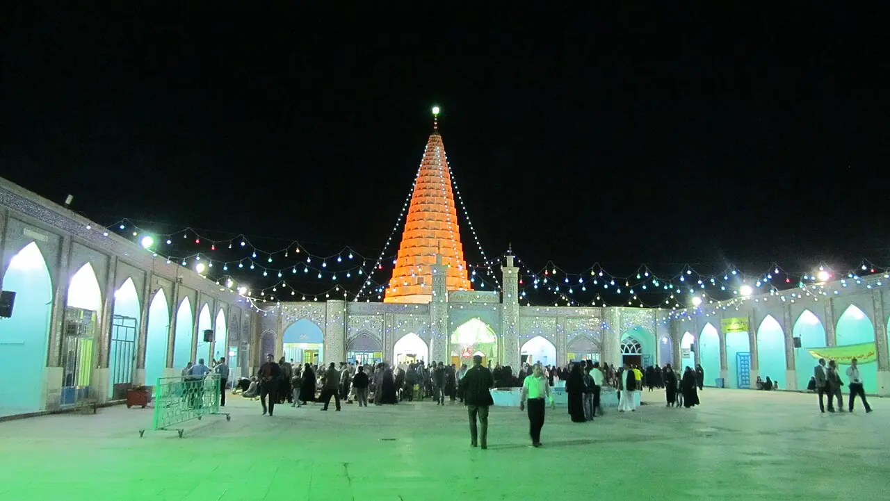 حیاط آرامگاه دانیال نبی در شب با گنبد مخروطی روشن و زائرانی در صحن