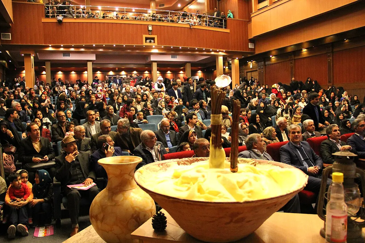 کاسه‌ی بزرگ کف‌بیخ سفید با دو چوب هم‌زدن، در برابر جمعیتی در یک سالن